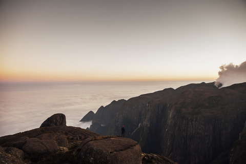 Fernblick auf einen Wanderer, der bei Sonnenuntergang auf einem Berg steht, lizenzfreies Stockfoto