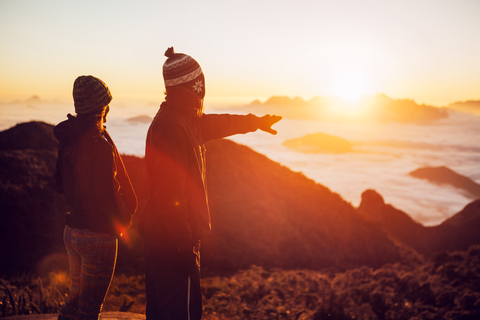 Mann, der mit einer Frau auf einem Berg steht, während die Sonne untergeht, lizenzfreies Stockfoto