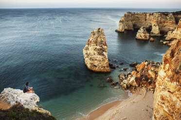 High angle view of man sitting on cliff while looking at sea - CAVF30646