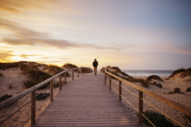 Distant view of hiker walking on footbridge at beach against sky during sunset - CAVF30665