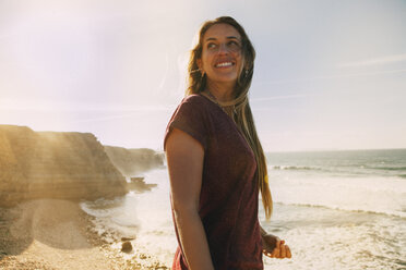 Smiling woman looking away while standing at beach against sky - CAVF30673