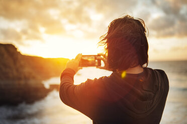 Rückansicht eines Mannes, der während des Sonnenuntergangs am Strand steht und fotografiert - CAVF30679