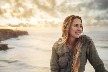 Smiling woman looking away while sitting against sea - CAVF30681