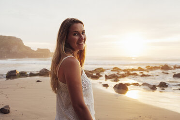 Porträt einer lächelnden Frau, die bei Sonnenuntergang am Strand steht - CAVF30701