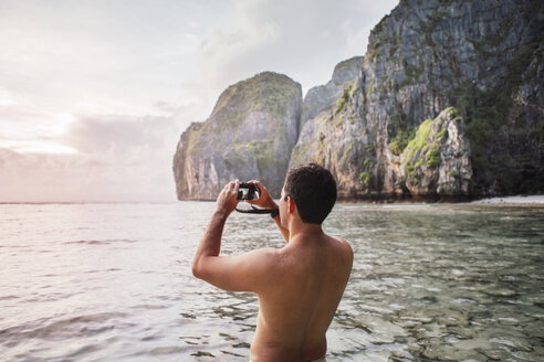 Rear view of shirtless man photographing while standing at beach - CAVF30706