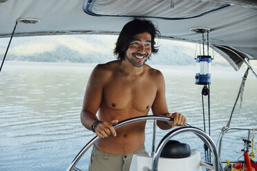 Glücklicher Mann ohne Hemd, der wegschaut, während er ein Boot auf dem Meer segelt - CAVF30711