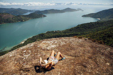 High angle view of woman relaxing on mountain by sea during sunny day - CAVF30712