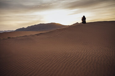 Rear view of woman photographing through mobile phone at desert during sunset - CAVF30720