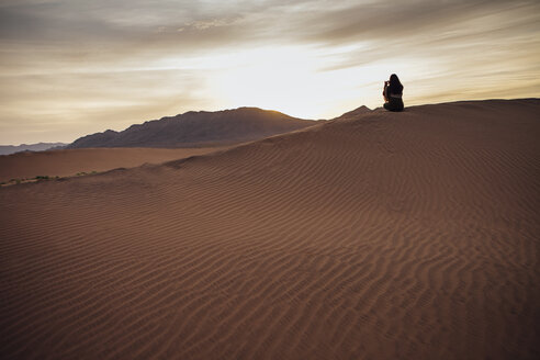 Rückansicht einer Frau, die mit ihrem Handy in der Wüste bei Sonnenuntergang fotografiert - CAVF30720