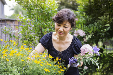 Ältere Frau hält Blumen bei der Gartenarbeit im Hinterhof - CAVF30803