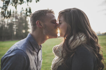 Couple kissing while standing on grassy field against sky - CAVF30813