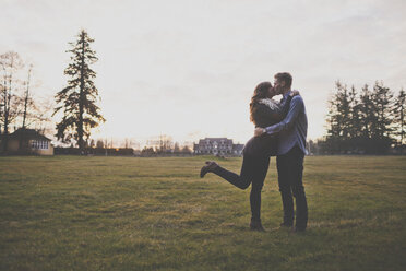 Romantisches Paar, das sich küsst, während es auf einem grasbewachsenen Feld vor dem Himmel steht - CAVF30814