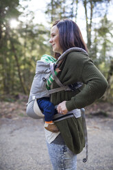 Seitenansicht einer Mutter mit ihrem Sohn in einer Babytrage auf dem Fußweg - CAVF30827