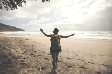 Rear view of mother with arms outstretched carrying son in baby carrier at beach against cloudy sky - CAVF30851