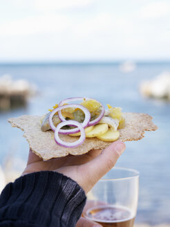 Close- up of hand holding crispbread with pickled herring and onion rings - FOLF02804