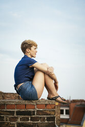 Junge blonde Frau sitzt auf dem Dach bei Sonnenuntergang - FOLF02900