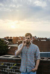 Junger blonder Mann raucht auf dem Dach bei Sonnenuntergang - FOLF02905