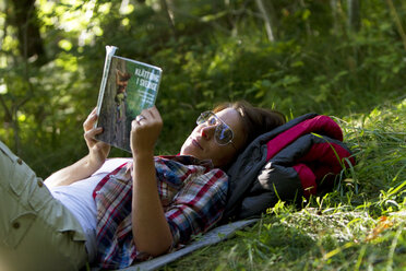 Female hiker lying on grass and reading guidebook - FOLF02918