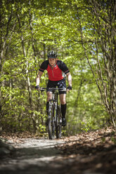 Mature man riding on mountain bike through forest - FOLF02939