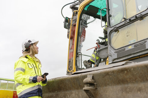 Frau spricht mit Mann in Erdbewegungsmaschine auf Baustelle - FOLF03221