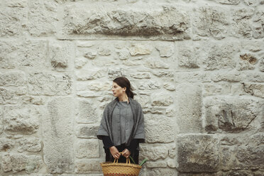 Junge Frau steht an einer Steinmauer und hält einen Korb - FOLF03269