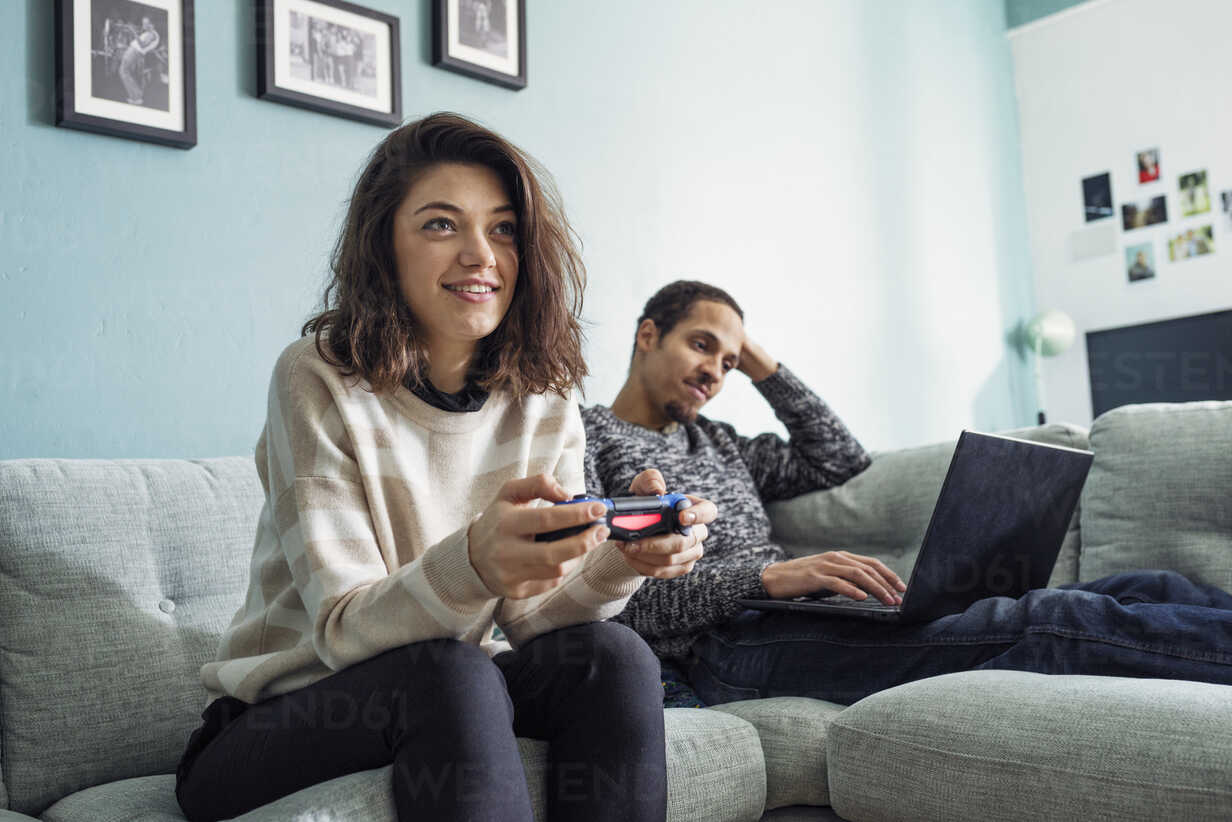 Young woman playing video games and young man using laptop in living room  stock photo