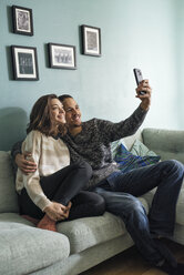Junges Paar sitzt auf dem Sofa im Wohnzimmer und macht ein Selfie mit dem Smartphone - FOLF03326