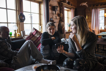 Junge Frau zeigt Freunden in einer Blockhütte ihr Smartphone - FOLF03331