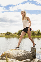Teenage girl walking on rocks by river - FOLF03336