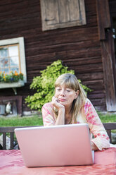 Frau arbeitet an einem Laptop vor einem Haus - FOLF03390