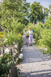 Frau zu Fuß mit Fahrrad entlang des Weges im Garten - FOLF03393