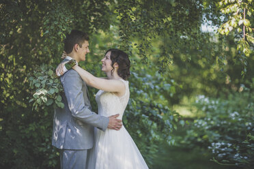 Happy newlywed couple embracing by branches in forest - CAVF30896