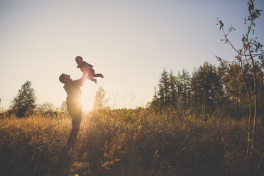 Father lifting son while standing on field against sky during sunset - CAVF30904