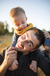 Verspielter Vater trägt seinen Sohn auf den Schultern auf einem Feld - CAVF30906