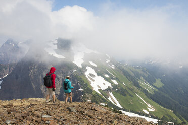 Rear view of hikers looking at view while standing on mountain against cloudy sky - CAVF30919