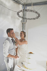 Verspielte Braut, die dem Bräutigam beim Hochzeitsempfang eine Torte ins Gesicht drückt - CAVF30926