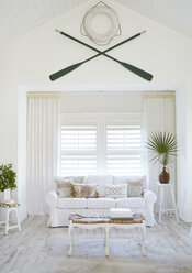 Oars and lifebelt hanging on wall above sofa at beach cottage - CAVF30942