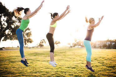 Friends exercising on grassy field on sunny day - CAVF30986