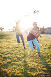 Female athletes running on grassy field on sunny day - CAVF30987