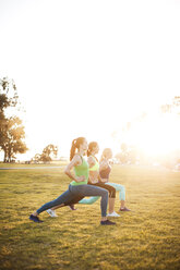 Women exercising on grassy field against clear sky - CAVF30989