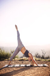 Woman practicing yoga on field against clear sky - CAVF31001