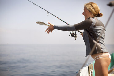 Glückliche Frau, die einen Fisch freilässt, während sie am Ufer steht - CAVF31048