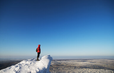 Hiker standing on snow covered mountain against clear blue sky - CAVF31101