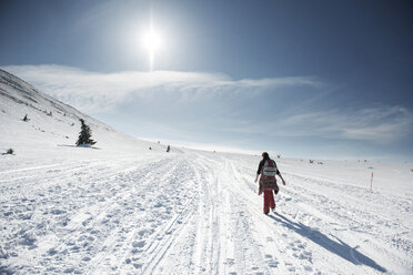 Rear view of woman walking on snow covered field against sky on sunny day - CAVF31110