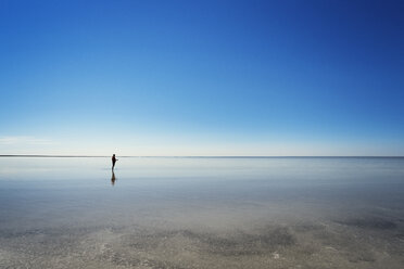 Mittlere Entfernung eines am Strand stehenden Mannes vor einem klaren blauen Himmel - CAVF31114