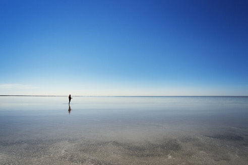 Mittlere Entfernung eines am Strand stehenden Mannes vor einem klaren blauen Himmel - CAVF31114