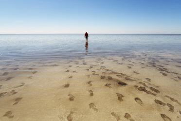 Mittlere Entfernung eines Mannes, der am Strand vor blauem Himmel spazieren geht - CAVF31117