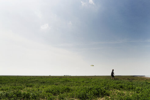 Mann wirft Flugscheibe auf grasbewachsenem Feld gegen den Himmel - CAVF31121
