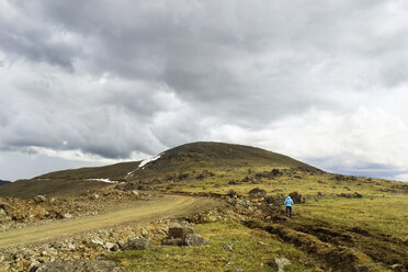 Rear view of woman walking on mountain against cloudy sky - CAVF31141