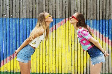 Cheerful female friends standing face to face against bamboo fence - CAVF31143